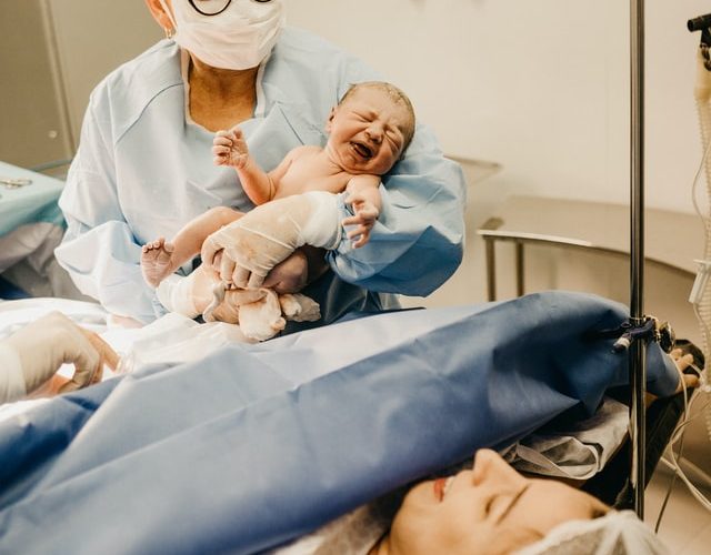 Lékařka ukazuje ženě dítě po provedení císařského řezu.
